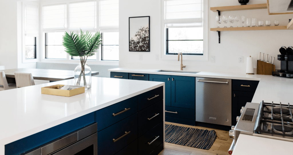 A kitchen featuring blue cabinets. The sun is shining through the window and there is a plant on the tan counter. The paint is likely interior. If you've accidentally used exterior paint inside, repainting with interior paint is best. 