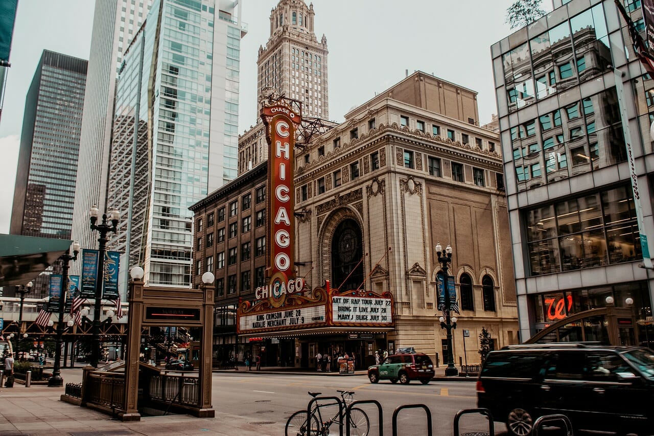 Image shows the Chicago theater, as well as other city aspects like a street, lamplights, bikes, and the opening to the subway. The theater is brown with red signage that reads "Chicago."